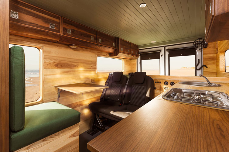 Interior of camper van with solid wood sky canbinets. Integrated kitchen on right side with sink and fireplace.