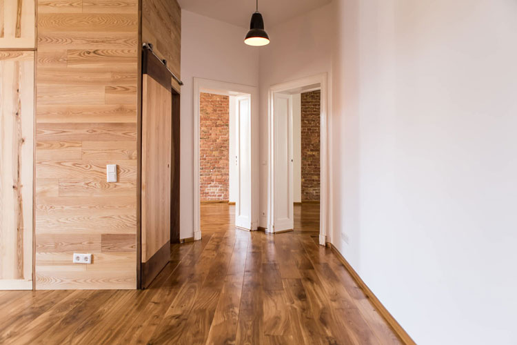 View on large room opening to two other rooms. Solid wood floor in dark wood. White wall on the right, wooden wall with slide door on left.