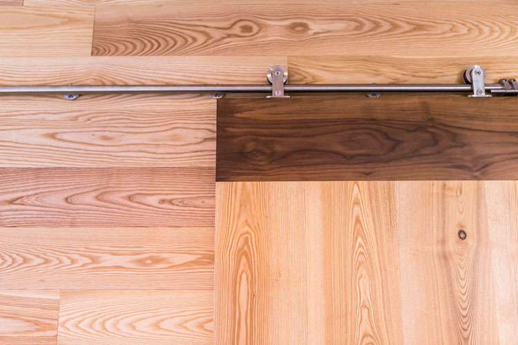Solid wood slide door on metal rail. Design pattern of dark and light wood. Detail view.