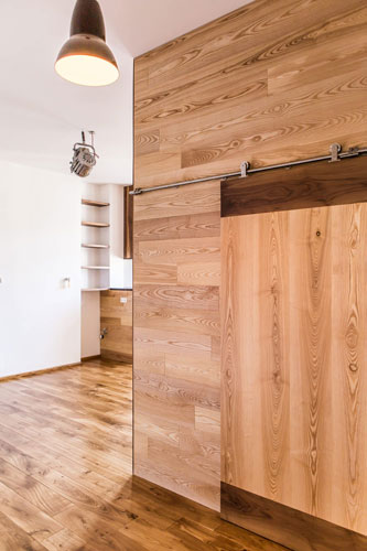 Detail view on solid wood slide door sliding on metal rail. Room opens op to living room with wooden shelves.